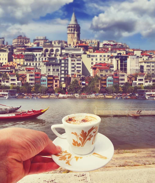 Hand with a cup of coffee with Istanbul riverside on a background. Travel concept