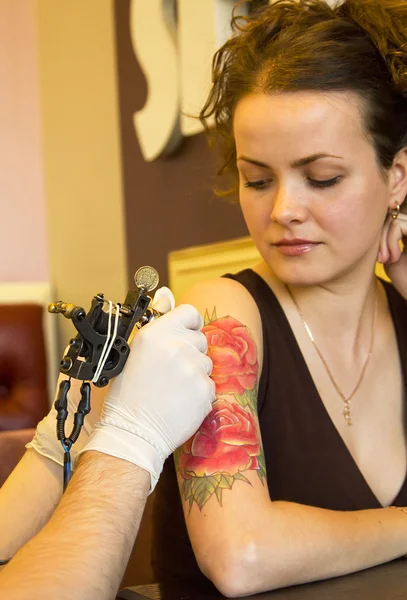 Tattooer showing process of making a tattoo on young beautiful hipster woman with red curly hair hand. Tattoo design in the form of rose