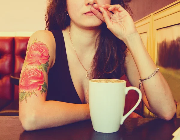 Young beautiful hipster tattooed woman with red curly hair at the bar with cup of coffee. Vintage style picture
