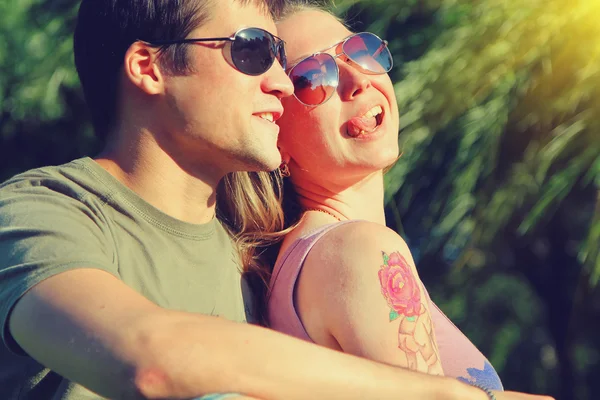 Young smiling couple in sunglasses sitting in a park in sunny day. friendship, leisure, summer concept. Vintage style toned picture