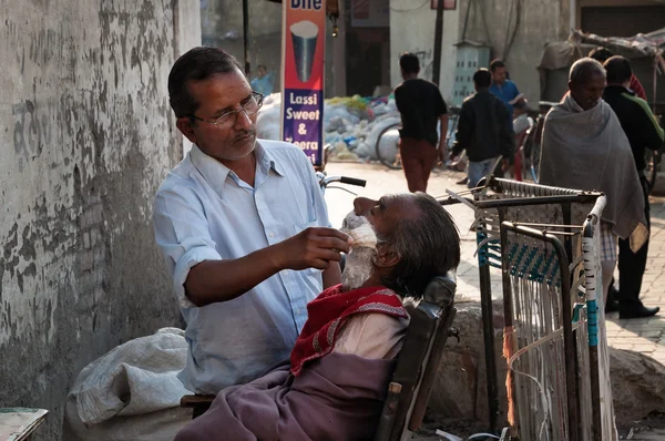 Street barber shaving a man on the street in Amritsar. India