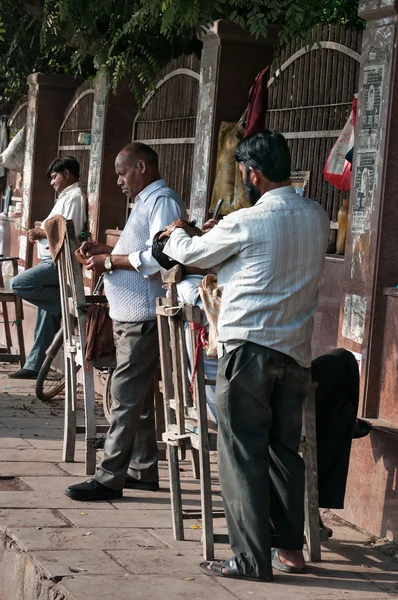 Street barbers shaving men on the street in market. Agra. India