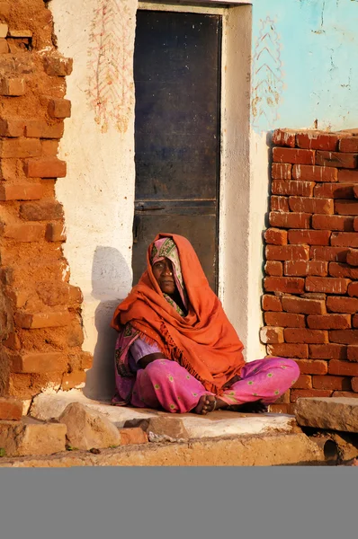 Indian woman in orange sari sits on a house porch