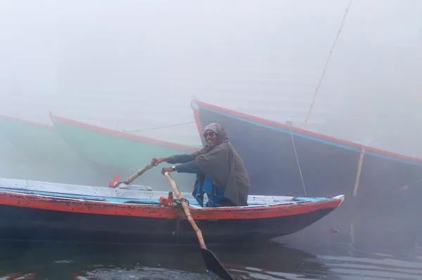Indian man sailing on the boat on sacred river Ganges at cold foggy winter morning