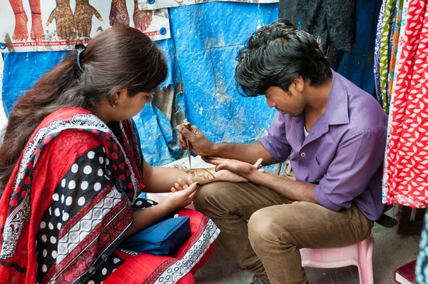 Indian man painting Henna paste on woman\'s hand at the Russell market in Bangalore