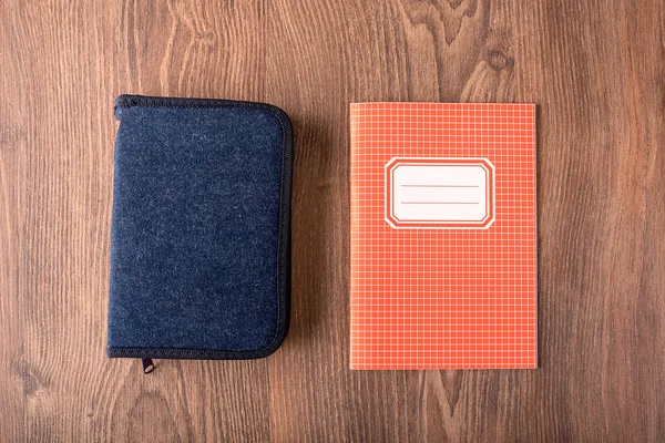 Squared exercise book and pencil case on wooden background