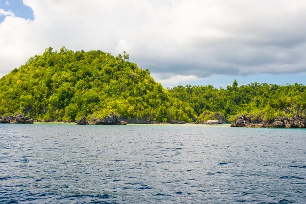 Rocky coastline of island spotted by islets and covered by dense lush green jungle in the colorful sea of the remote Togean Islands (or Togian Islands), Central Sulawesi, Indonesia.