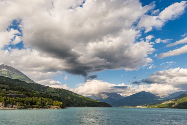 Blue lake amid mountain range and dramatic sky in idyllic uncontaminated environment once covered by glaciers. Dramatic sky, summer season, wide angle view.