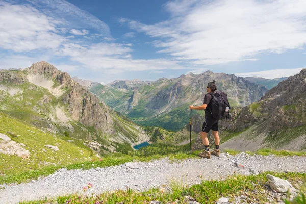 Backpacker hiking on footpath and looking at expansive view from the top. Summer adventures and exploration on the Italian French Alps.