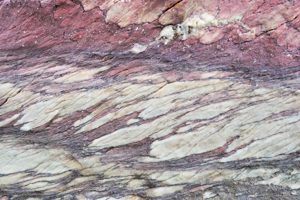 Close up of colorful rock surface, natural background, pattern and texture. Metamorphic white quartzite folded and fractured together with red coarse sandstone, due to the power of geologic crustal mo