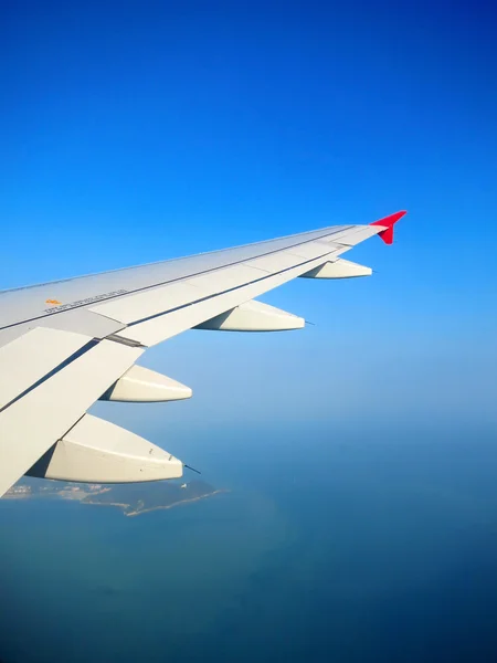 Plane wing in a blue sky above tropical island