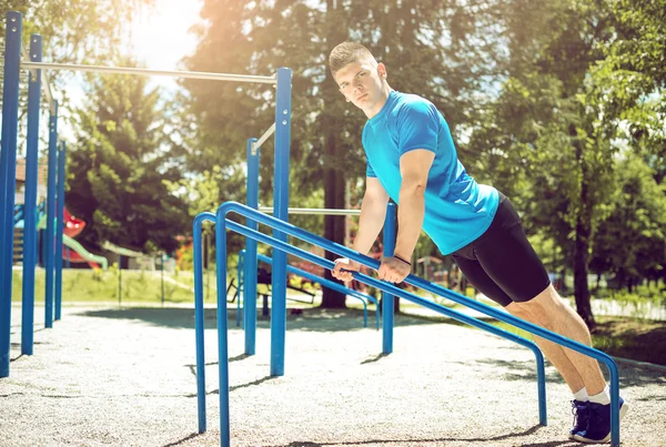 Man doing push-ups outdoor on metal bars.