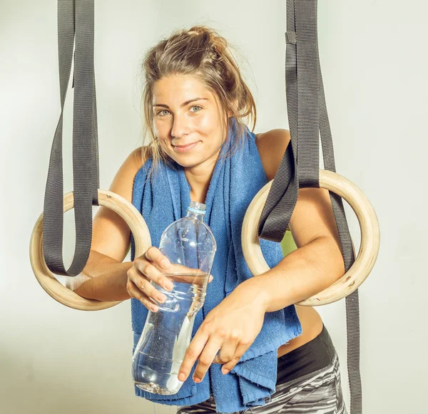 Tired woman with ring gymnastic equipment holding bottle of wate