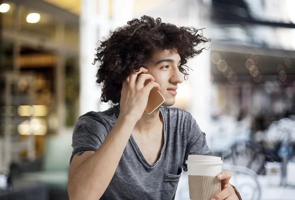 Young man talking phone and drinking coffee in cafe