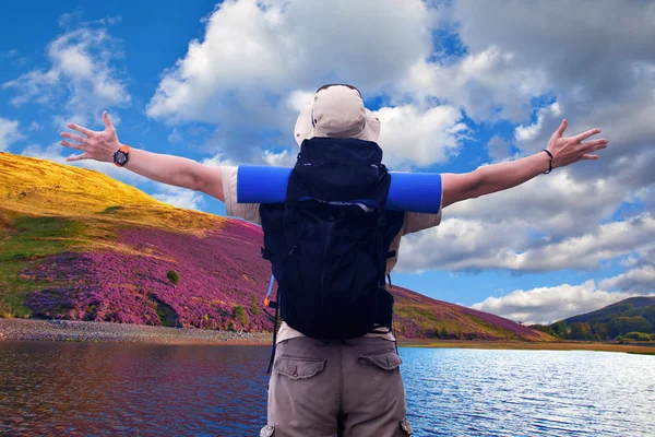 Hiker with black rucksack spreads hands expressing happiness at beautiful nature location