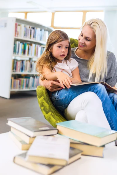 Mother with little girl read book together in library
