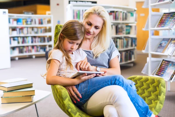 Mother with daughter look at their touchpad tablet device togeth