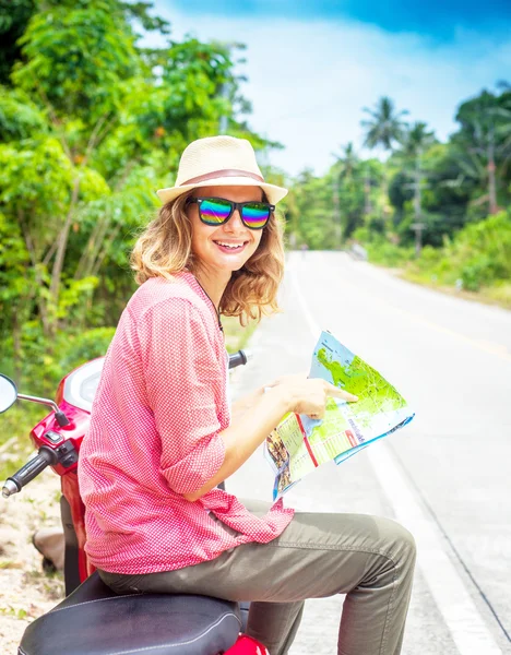 Beautiful young woman with map in hand and a motorbike on the ro