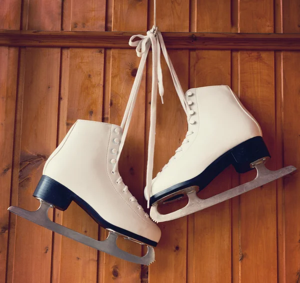 White ice skates for figure skating, hanging on a wooden backgro