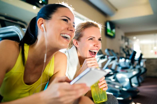 Attractive fit women in gym with smart phone laughing