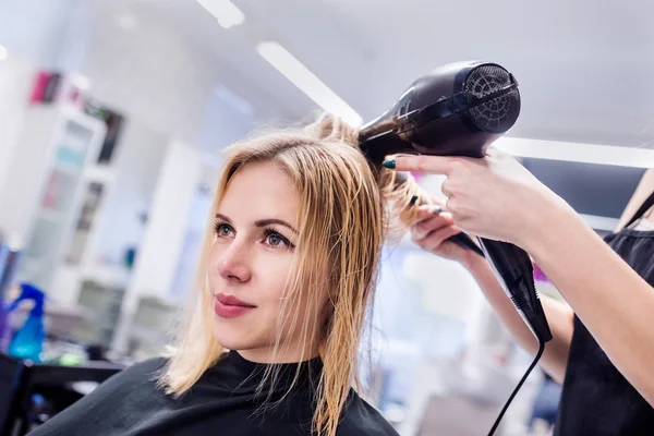 Unrecognizable hairdresser drying hair of her beautiful young cl