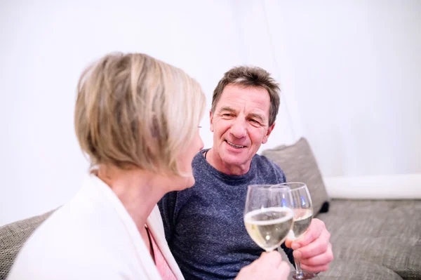 Senior couple sitting in living room, drinking champagne