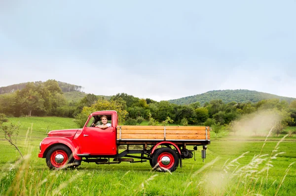 Young man inside red vintage pickup truck, green nature