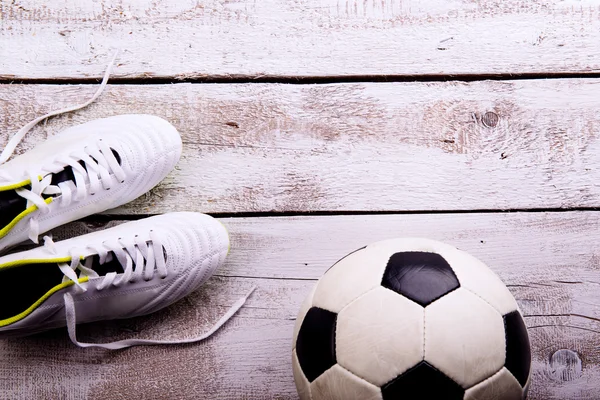 Soccer ball, cleats on white wooden floor, studio shot