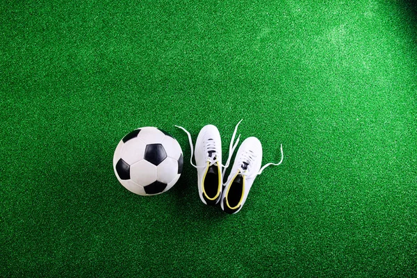 Soccer ball and cleats against green artificial turf, studio sho