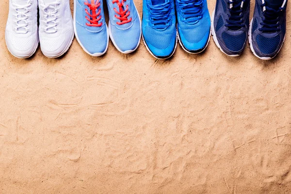 Various sports shoes in a row against sand, studio shot