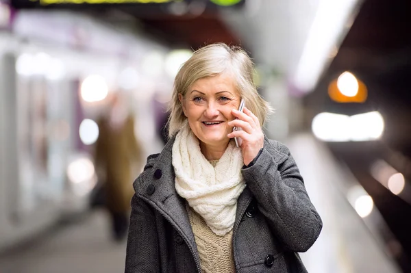 Senior woman at the underground platform, talking on phone