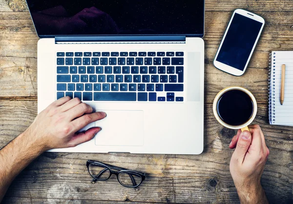 Male hands using laptop and drinking coffee.