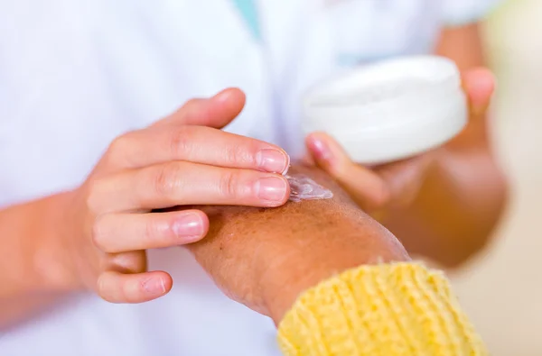 The carer rubbing the elderly woman\'s hand  with cream