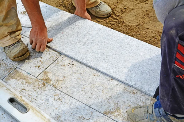 Workers laying granite block paver in place