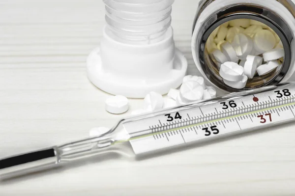 Close up of medicine white tablets and thermometer on a wooden table