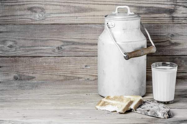 Some bread, a milk glass and a  milk can  on a wooden background