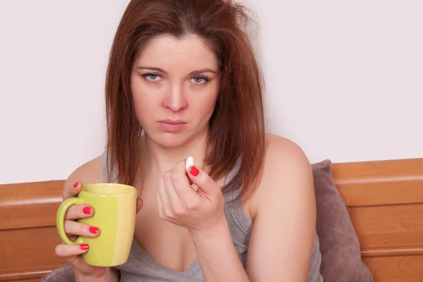 Sick woman in frustration. Closeup image of young woman with red nose holding a cup of tea while sitting in bed with copy space