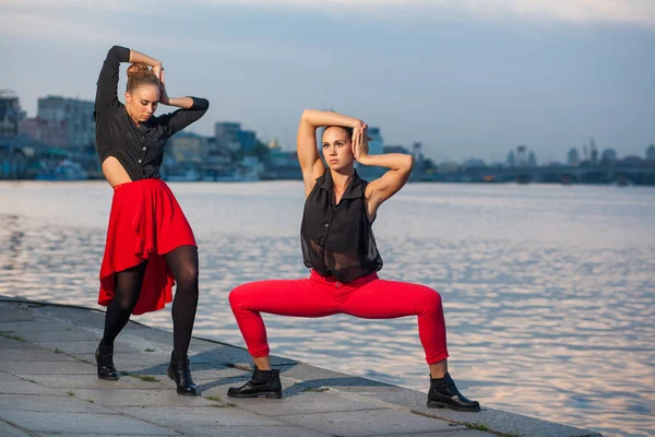 Two young beautiful twin sisters are dancing waacking dance in the city background near river.