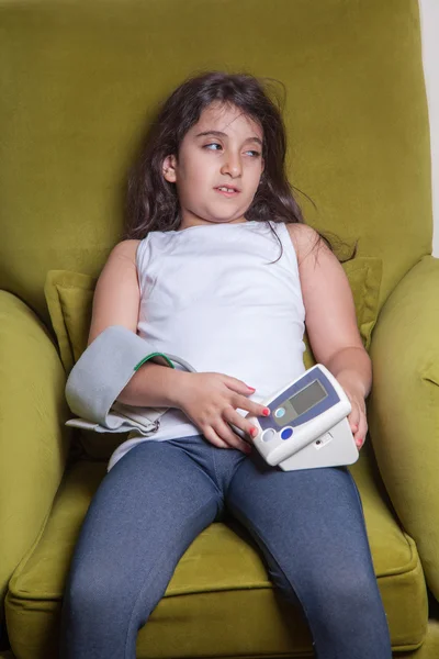 Small middle eastern girl feeling sick bad and holding digital blood pressure device.