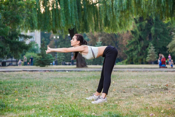 Young happy beautiful sexy girl is stretching in the park garden. people background. with dark hair and black and white sport suit and happiness and smile. on summer or autumn time season.