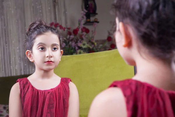 Small beautiful arab middle eastern girl with pretty red dress and lips posing and looking at herself in mirror. 8-10 years.