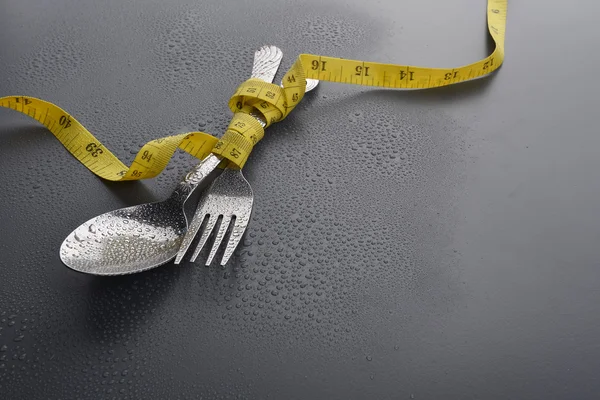 Lowlight key of spoon, fork and Yellow measuring tape with water drop on grey background