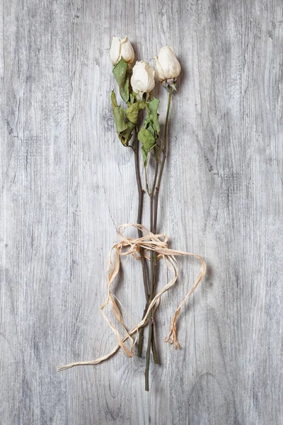 Dry white roses tied on its stem in the foreground on table