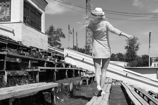 Blonde walking woman mode wearing hatl in front of old stadium s