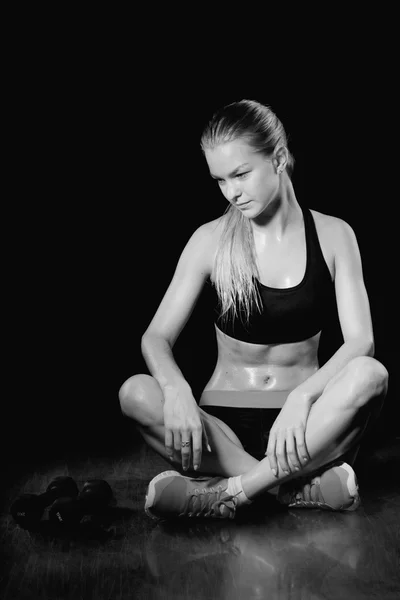 Female fitness model resting. Black background