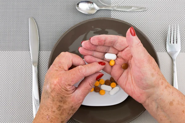 Red nailed elderly hands picking pills from a plate