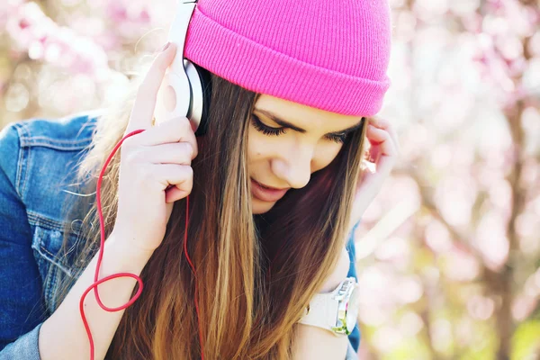 Close up portrait of a funny young swag girl on lush garden listening to music in earphones from smart phone mp3 player.