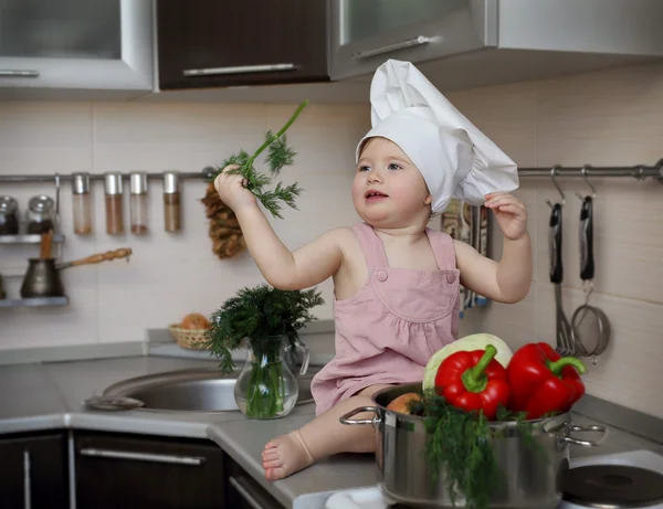 The child in the kitchen holding a sprig of dill