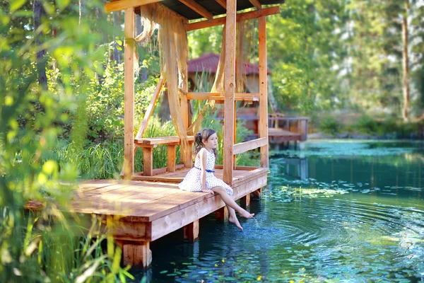 Girl sitting on a wooden bridge at the pond