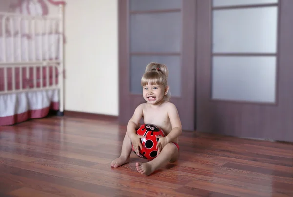 Little girl sitting on the floor in the nursery with the ball